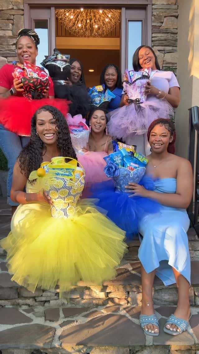 Women in monochromatic red, yellow, blue, pink, and purple outfits holding matching baskets.