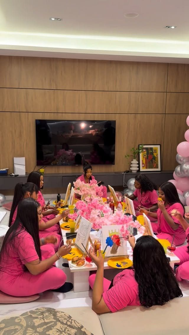 Women in pink pajamas painting on canvases at a pink themed party table.