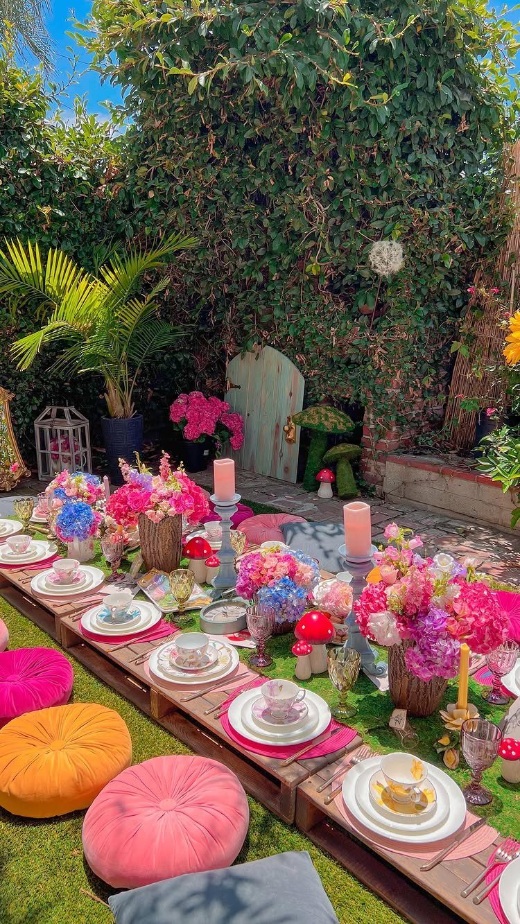Low wooden tea table with colorful flowers, pink plates, and bright floor poufs.