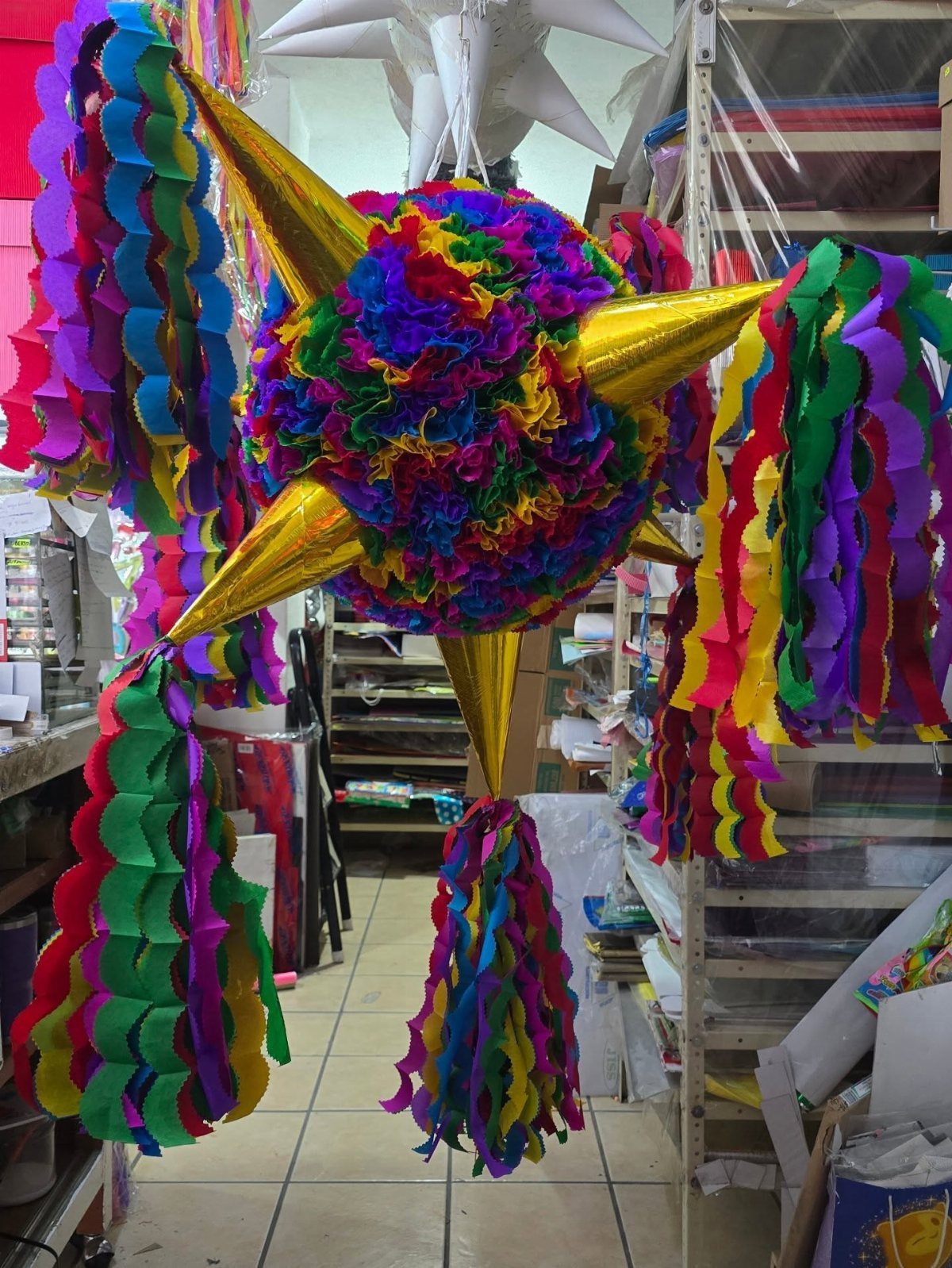 Star-shaped piñata with rainbow fringed center and gold points and colorful streamers.