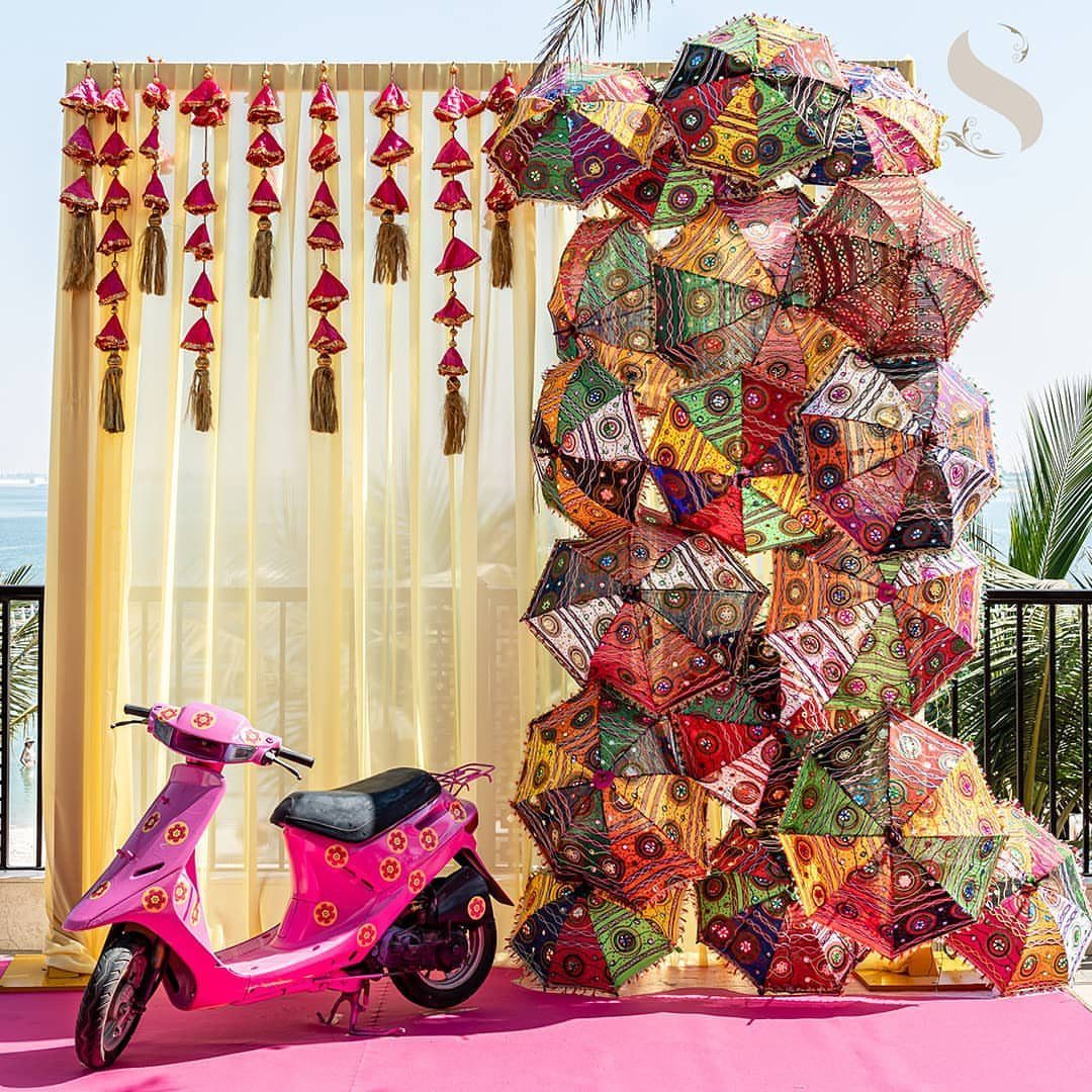 Pink floral scooter in front of a colorful umbrella wall and yellow curtain backdrop