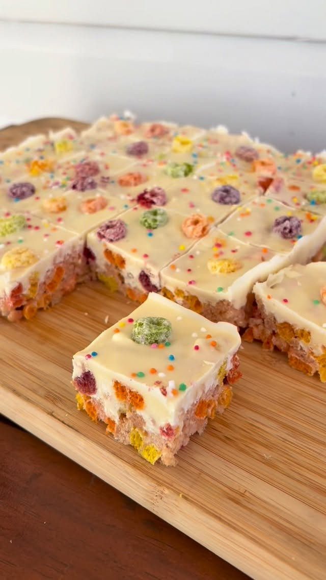 Colorful cereal treats with white topping and rainbow sprinkles on a wooden board.