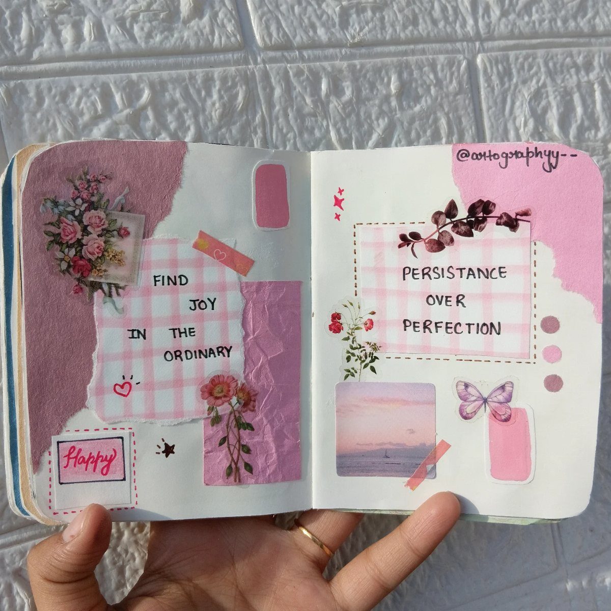 Open art journal with pink floral decorations and inspirational quotes held by a hand.