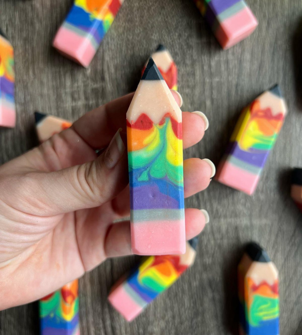 Rainbow colored soap bars shaped like pencils on a dark wooden background.