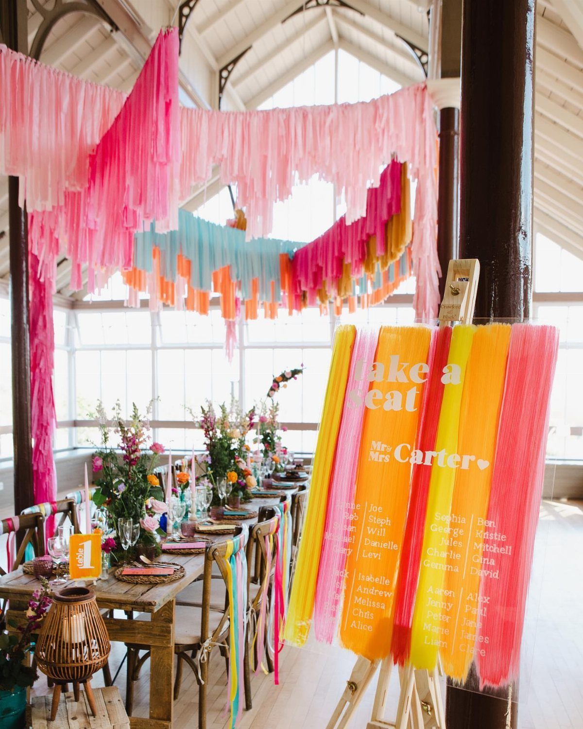 Colorful pink and orange streamers hanging over a decorated party table and seating chart.