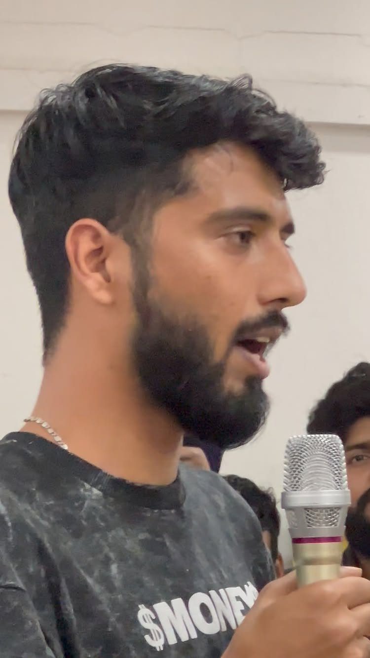 Man with a beard speaking into a microphone during a talent show performance.