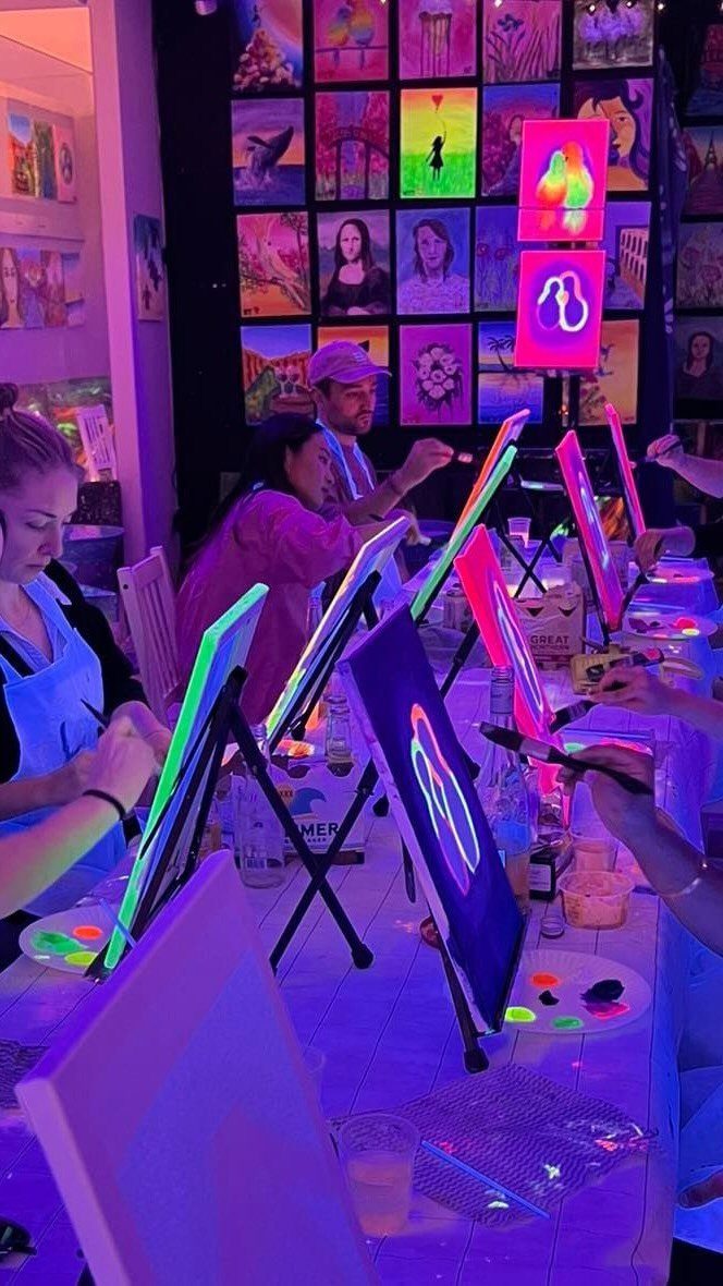 People painting neon canvases under UV blacklight at a creative corporate event.