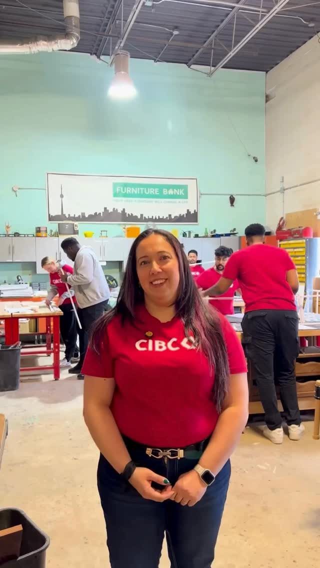 Woman in red CIBC shirt smiling in a furniture bank warehouse with colleagues.