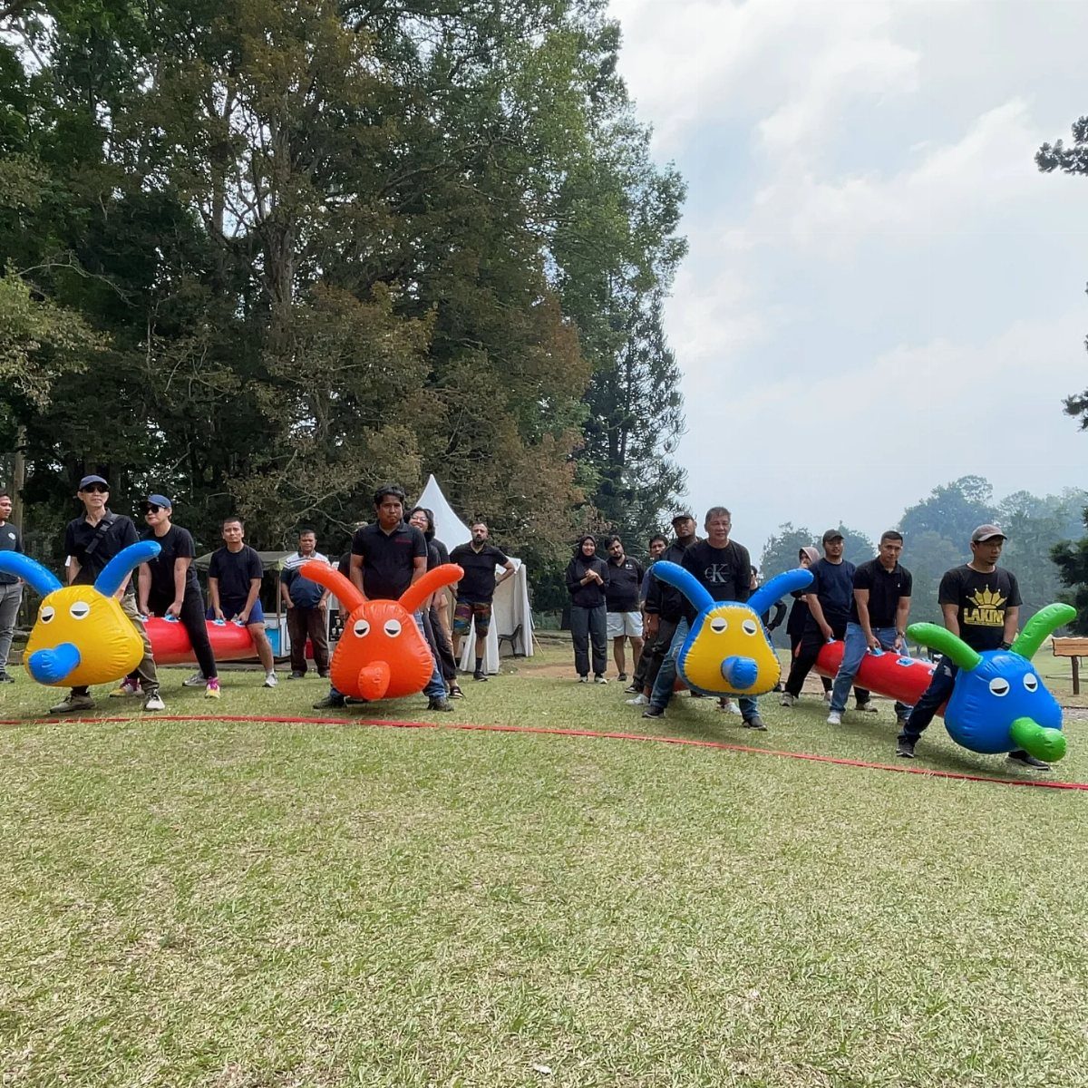 People in black shirts wearing colorful inflatable costumes during an outdoor corporate team-building event.