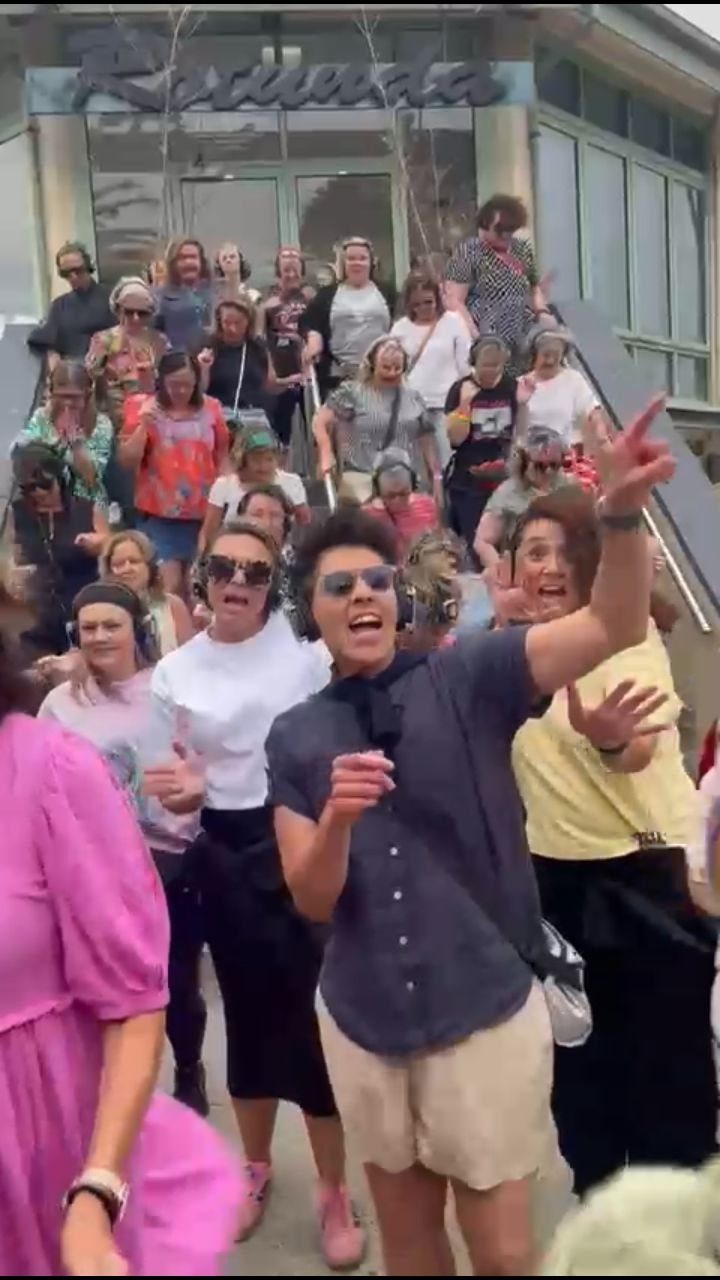 People wearing wireless headphones dancing and cheering while walking down outdoor stairs.