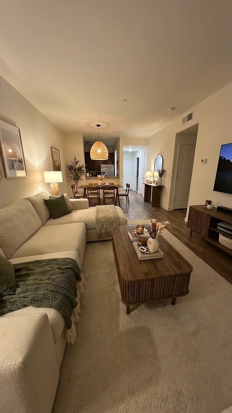 Beige sectional sofa with green throws and wooden coffee table in cozy apartment.