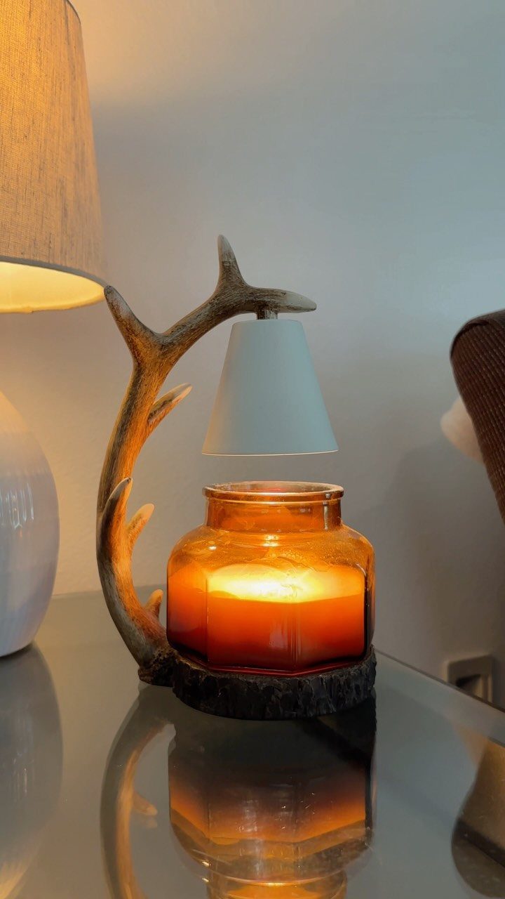 Scented candle in amber glass jar under a white ceramic wax warmer stand