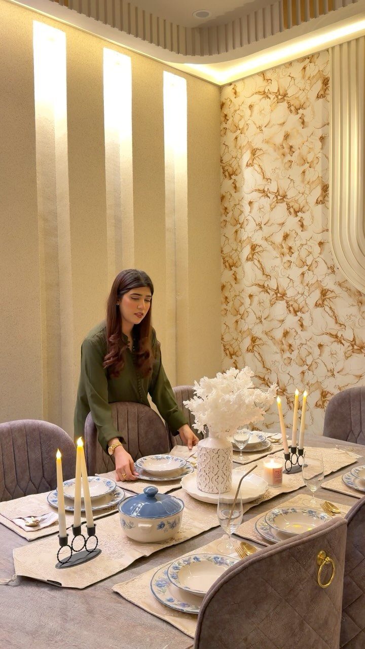 Woman standing by a dining table set with beige placemats and lit candles.