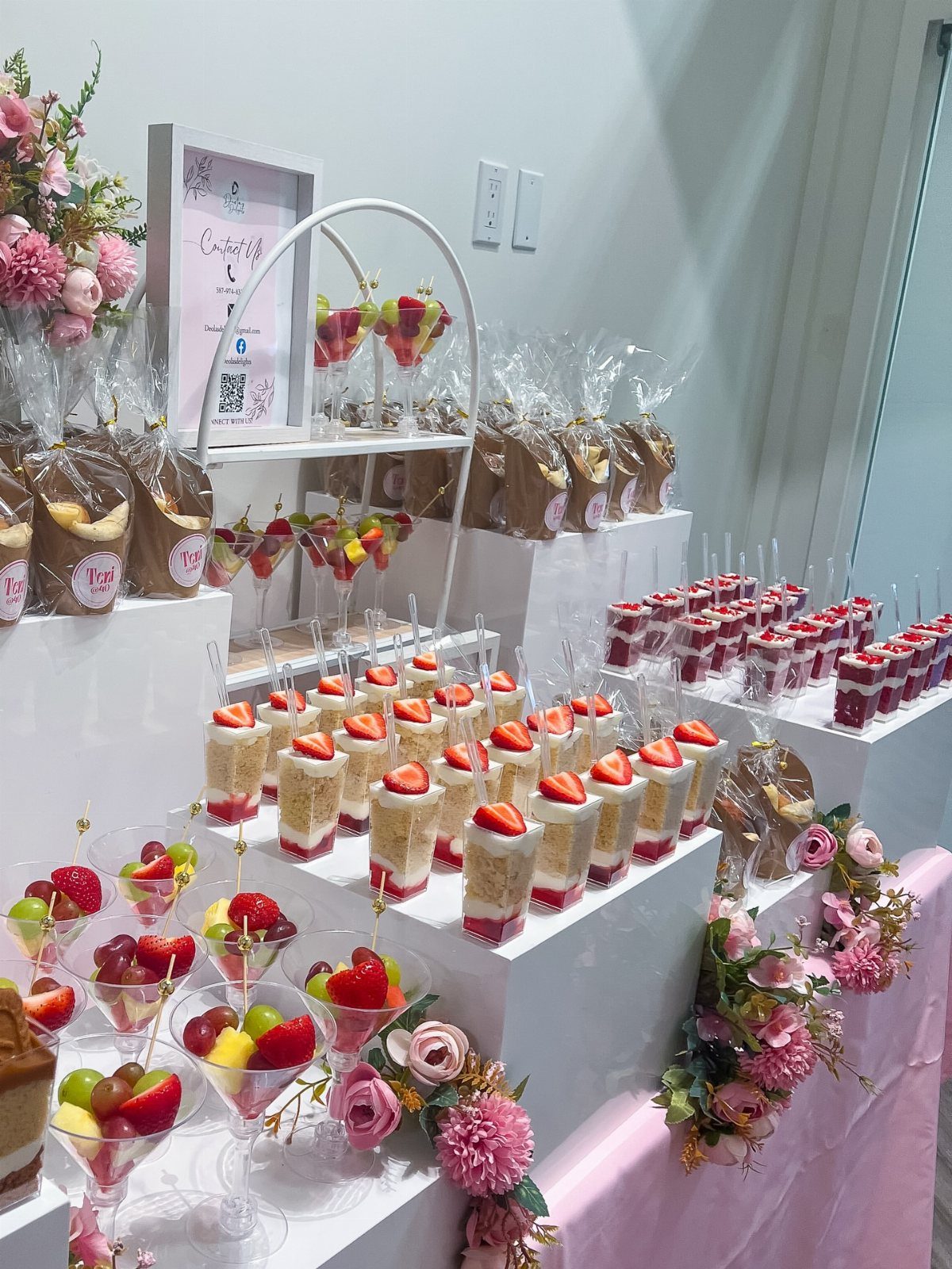 Dessert table display with strawberry cake cups, fruit parfaits, and pink floral decorations.