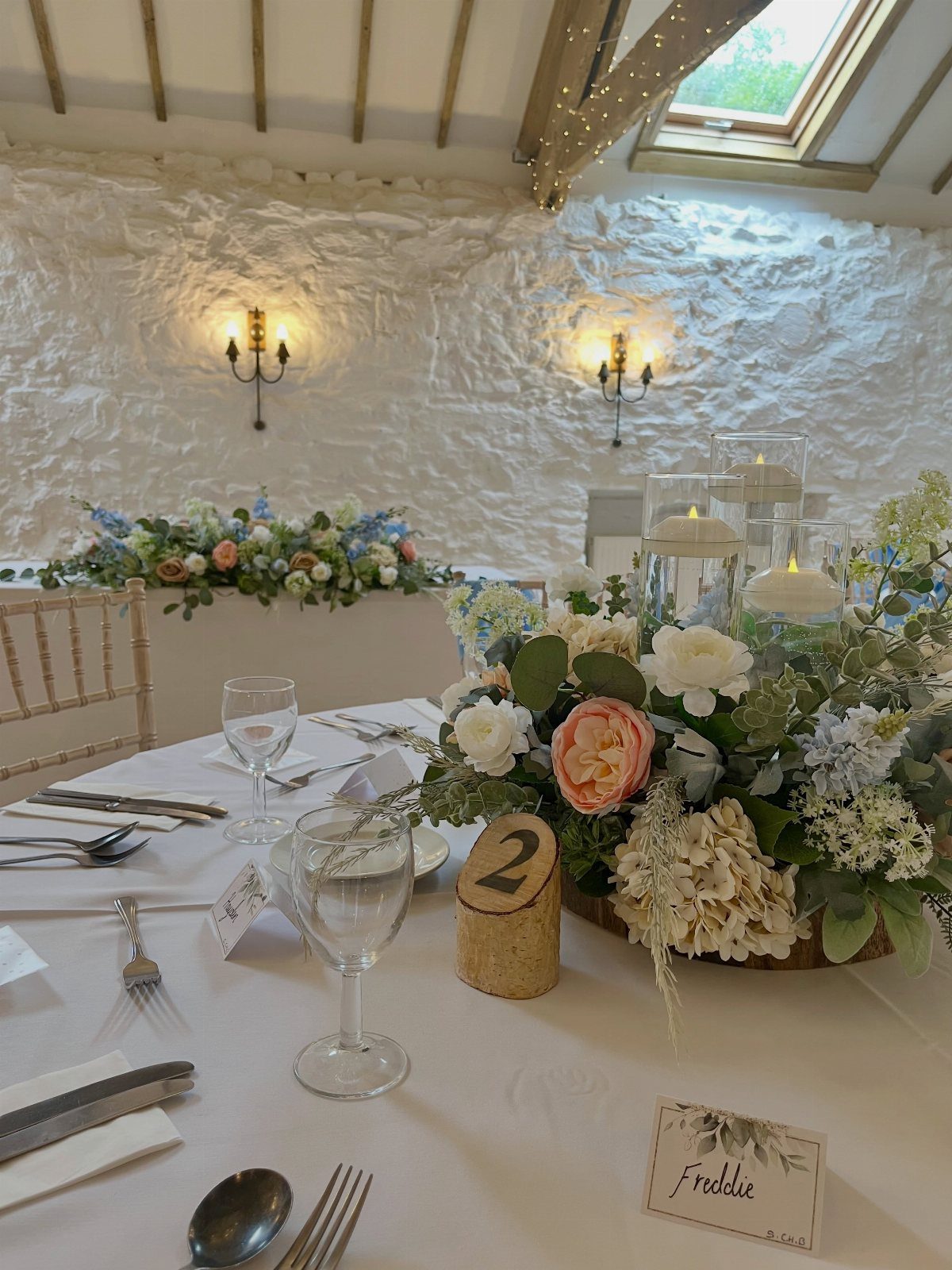 Floral centerpiece with white and peach roses and cylinder candles on a white table.