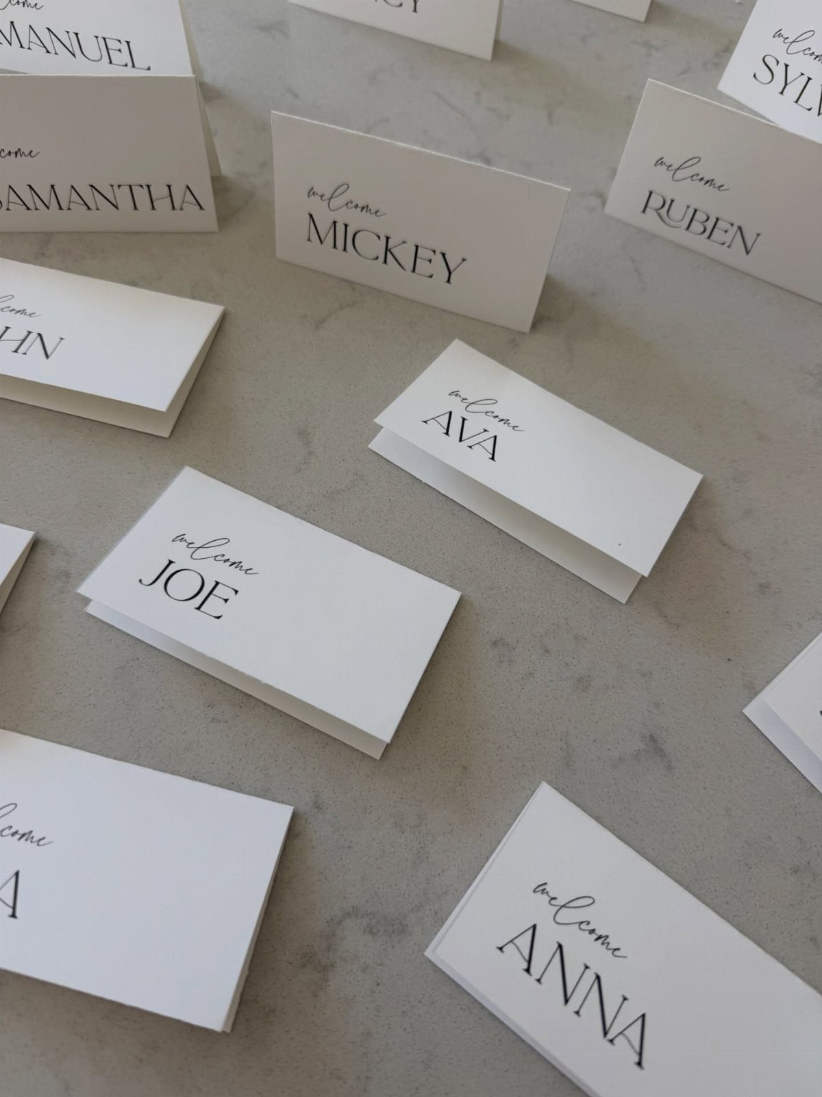 White folded place cards with black printed names on a grey stone surface.