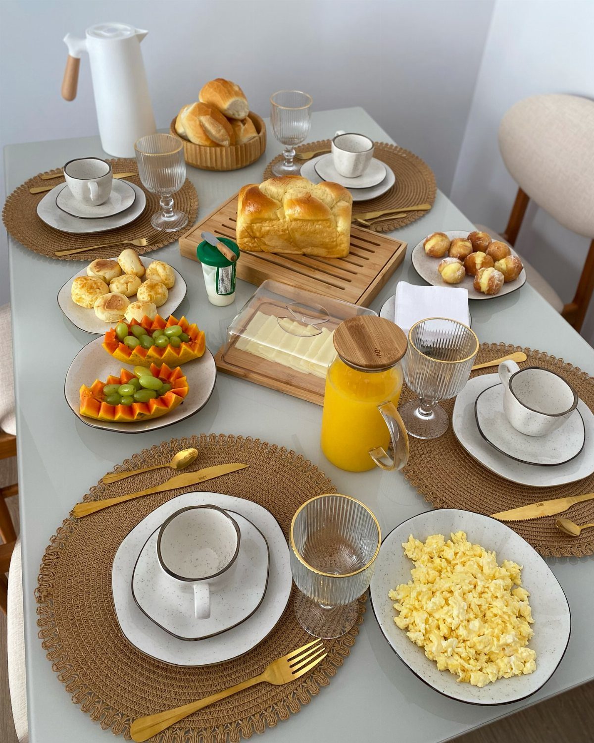 Breakfast table spread with eggs, fruit, bread, and orange juice on woven placemats.
