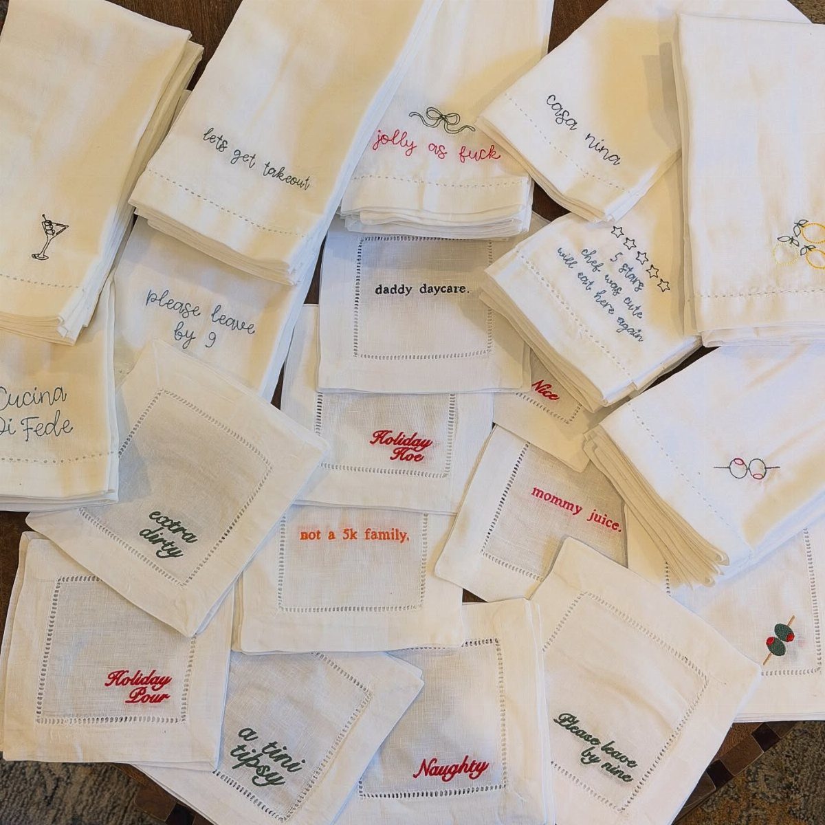 White linen dish towels with colorful embroidered phrases scattered on a brown surface.