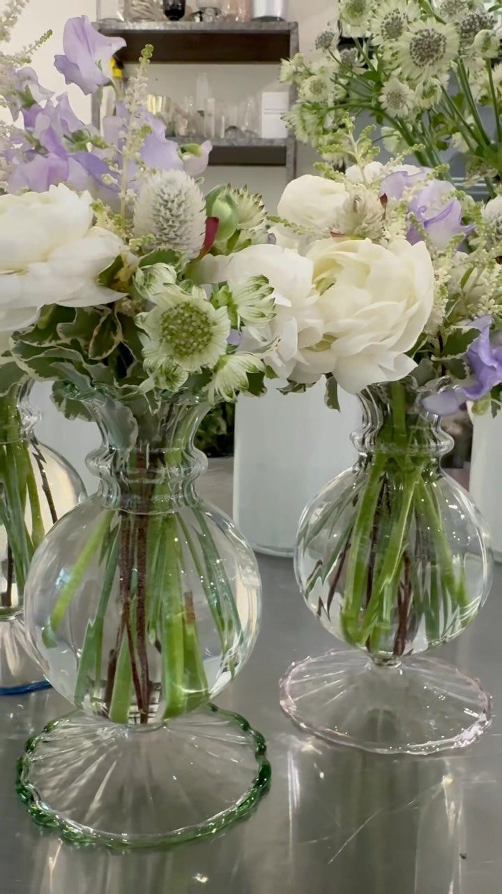 White and purple flowers arranged in clear glass vases on a reflective surface.