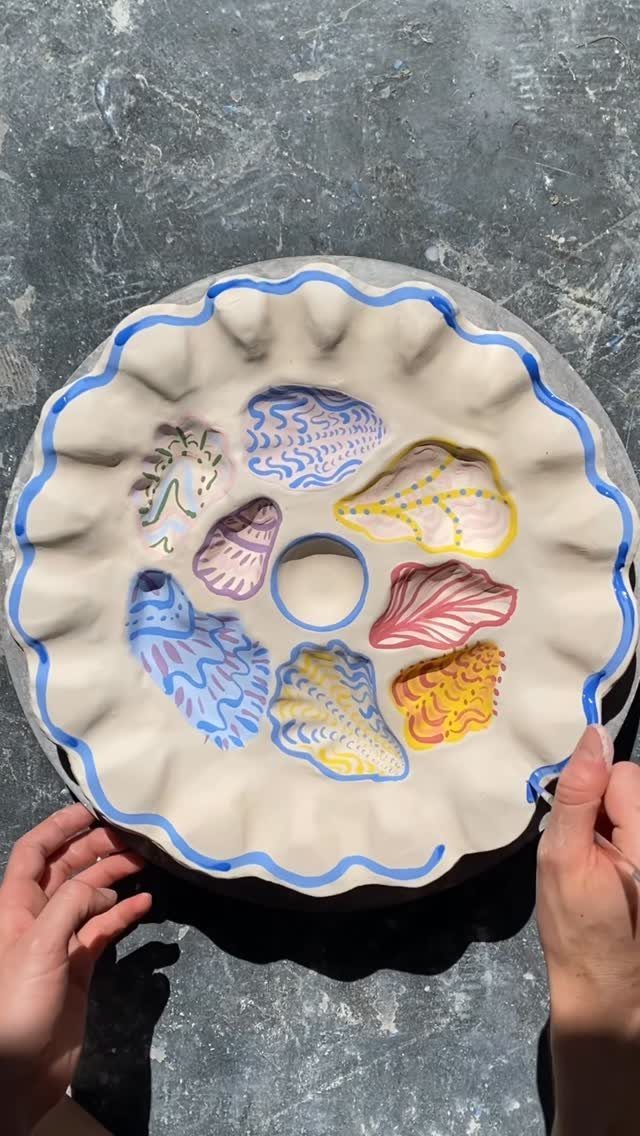 Hand-painted ceramic tart pan with colorful seashells held by two hands
