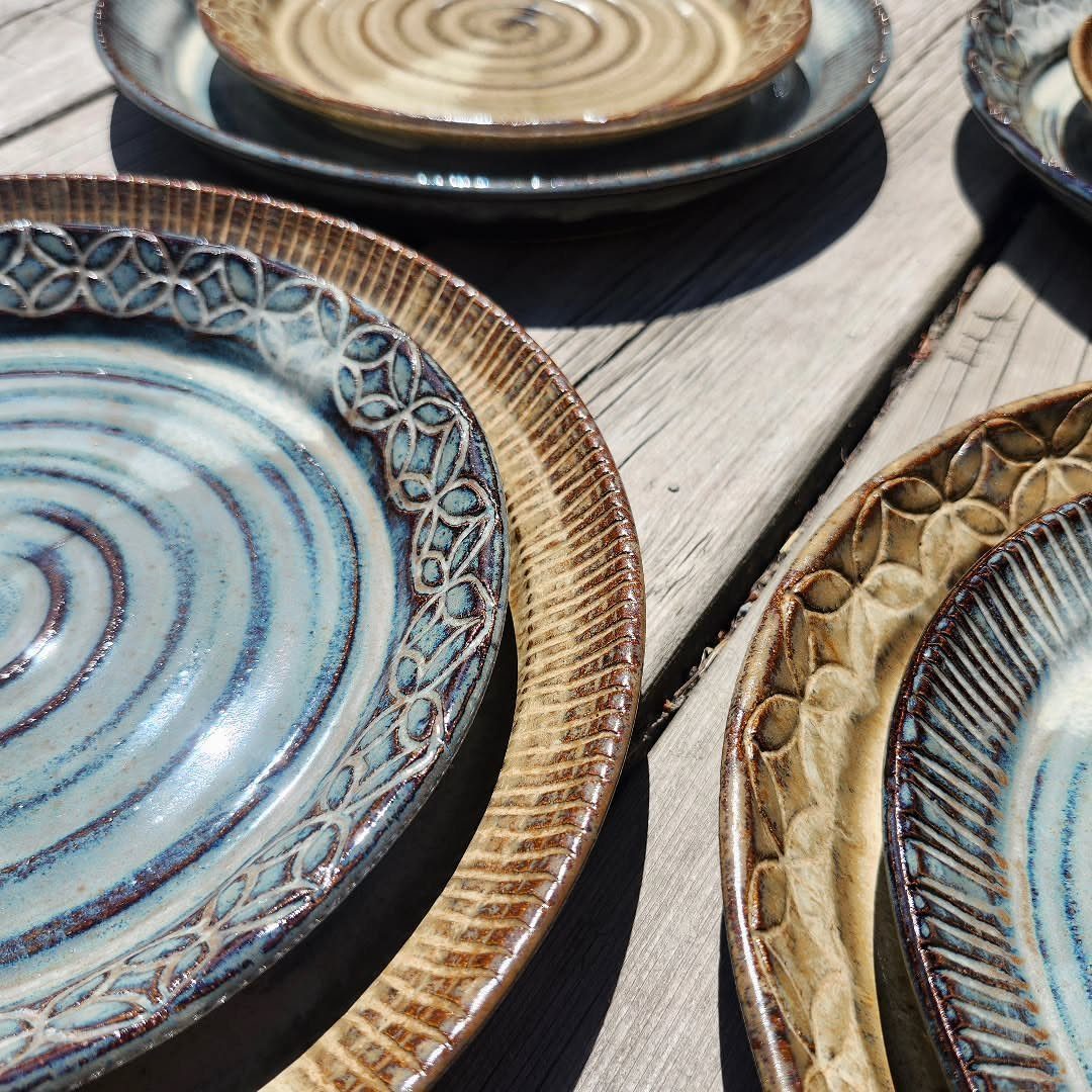 Handmade ceramic plates and bowls with blue and brown glazes on wooden planks