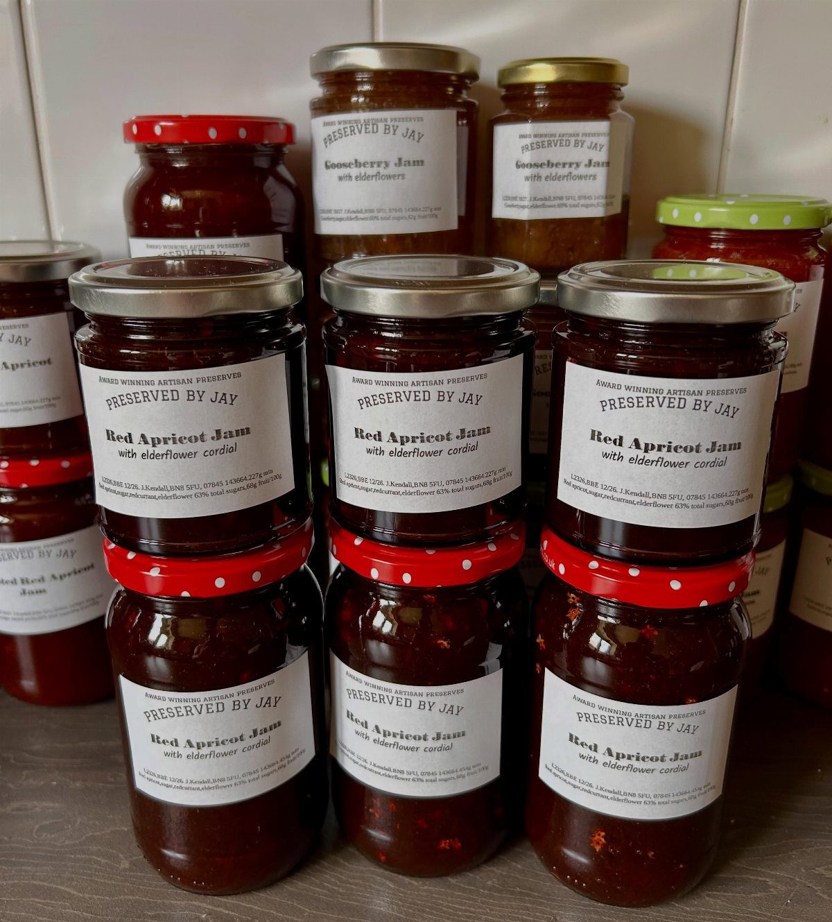 Glass jars of red apricot jam with white labels on a brown surface.