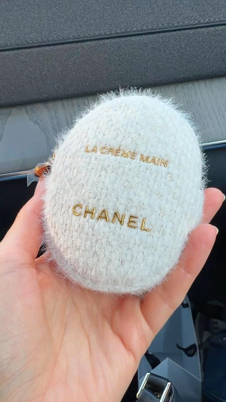 White fuzzy Chanel hand cream pouch held in a person's hand.
