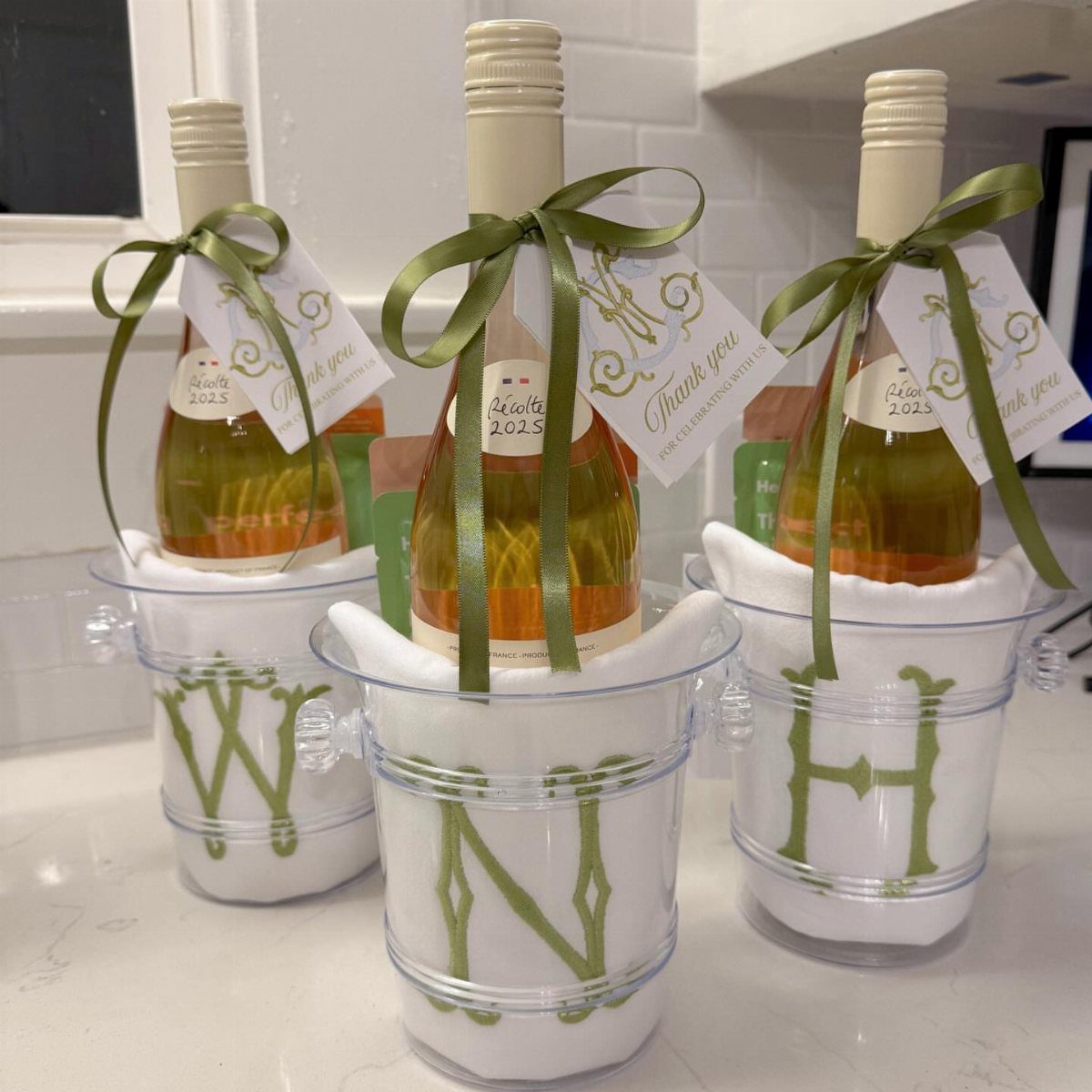 Three bottles of rosé wine in monogrammed buckets with green ribbons and tags.