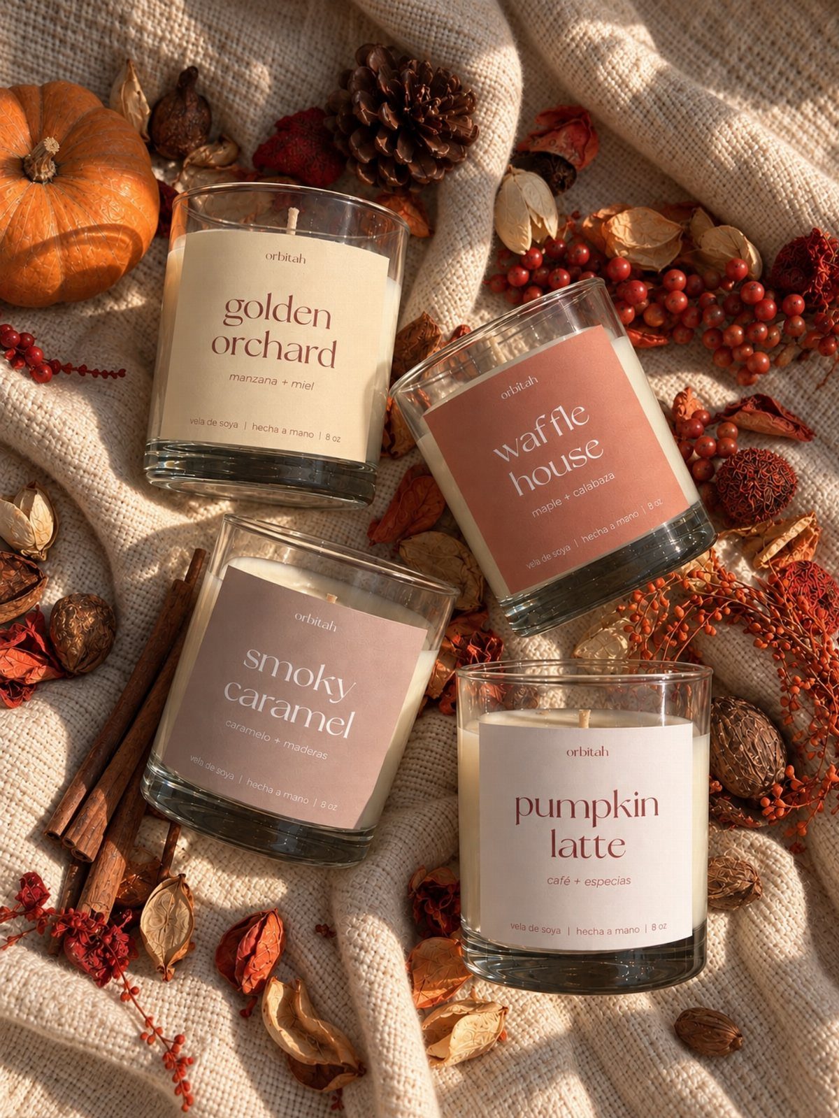 Four autumn-themed scented candles arranged with a pumpkin, cinnamon sticks, and pinecones.