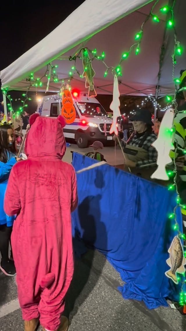 Person in pink bear costume fishing for candy at a decorated trunk-or-treat station.