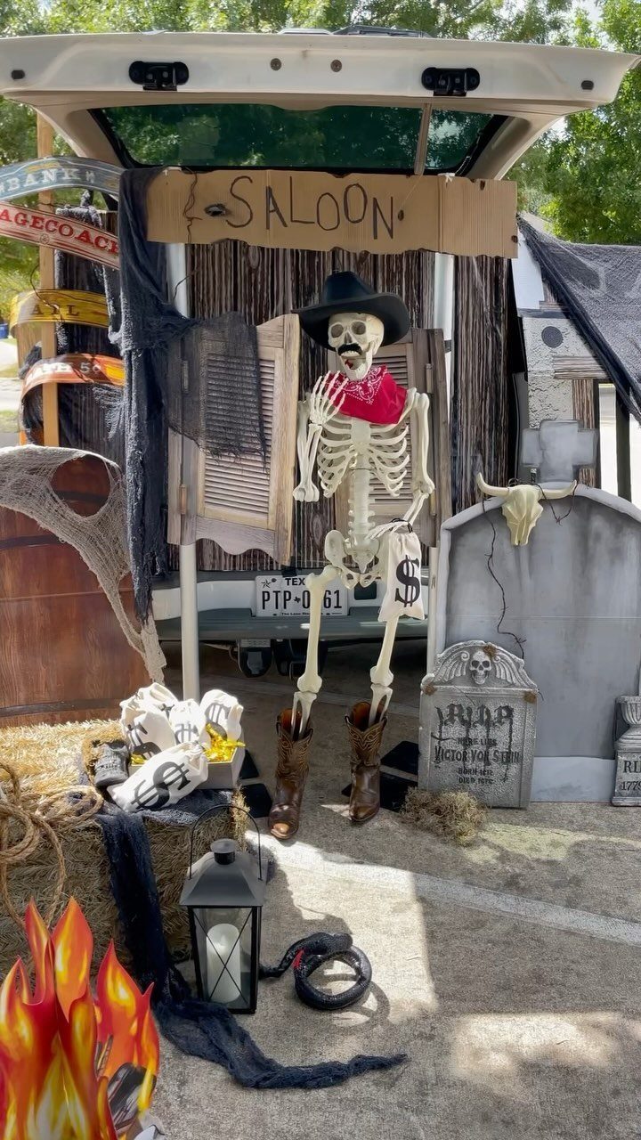 Skeleton cowboy in a saloon-themed car trunk with tombstones and hay bales.