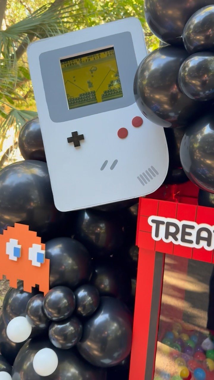 Handheld game console cutout and black balloons for a video game themed trunk.