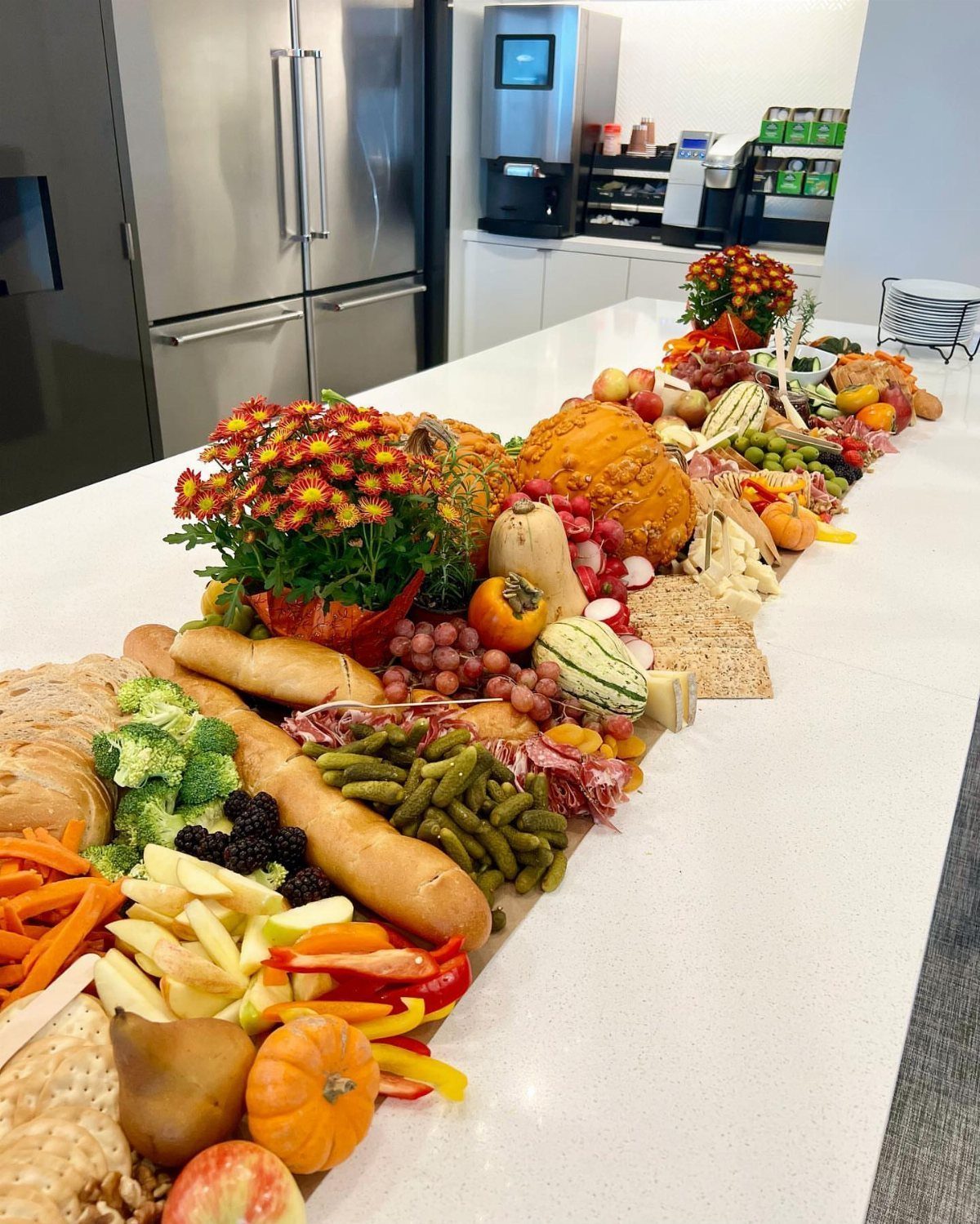 Autumnal charcuterie board with cheeses, fruits, vegetables, and small pumpkins on white counter.