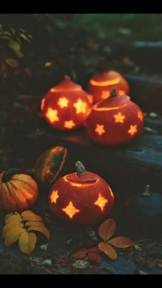 Glowing carved pumpkins with star patterns sitting among autumn leaves outdoors at dusk.