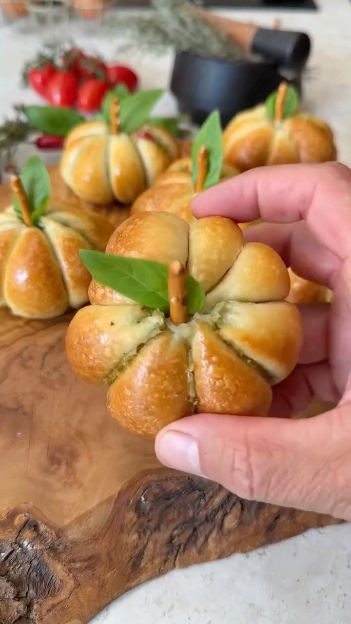 Pumpkin shaped bread rolls on a rustic wooden board with a hand holding one.