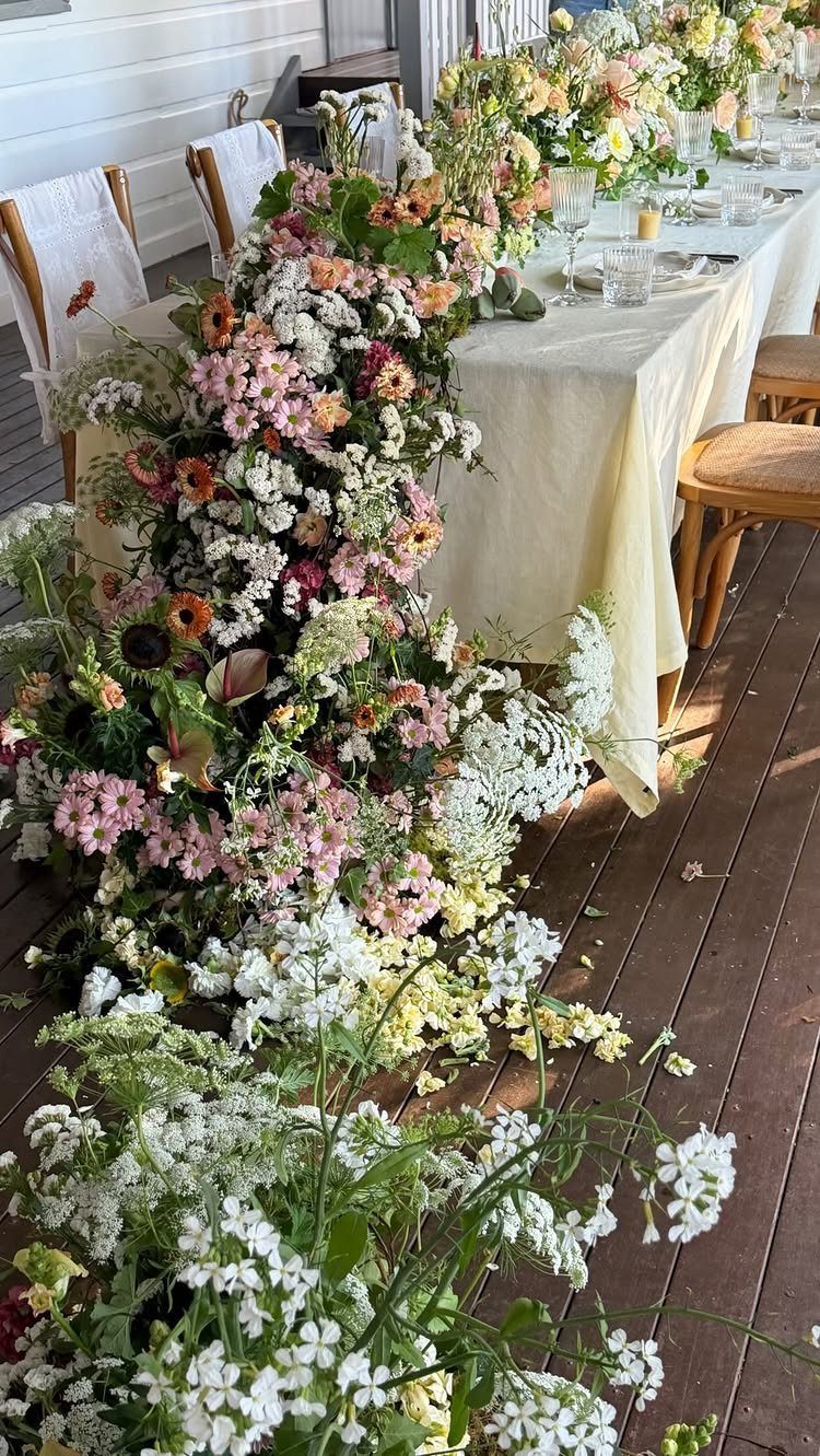 Cascading pink and white floral arrangement spilling from a cream-covered dining table.