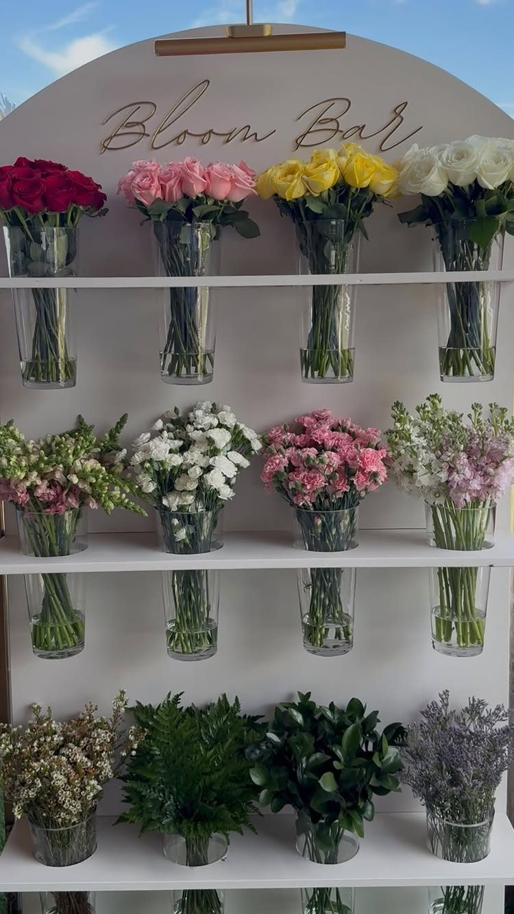 Bloom Bar station with colorful fresh flowers in glass vases on white shelves.
