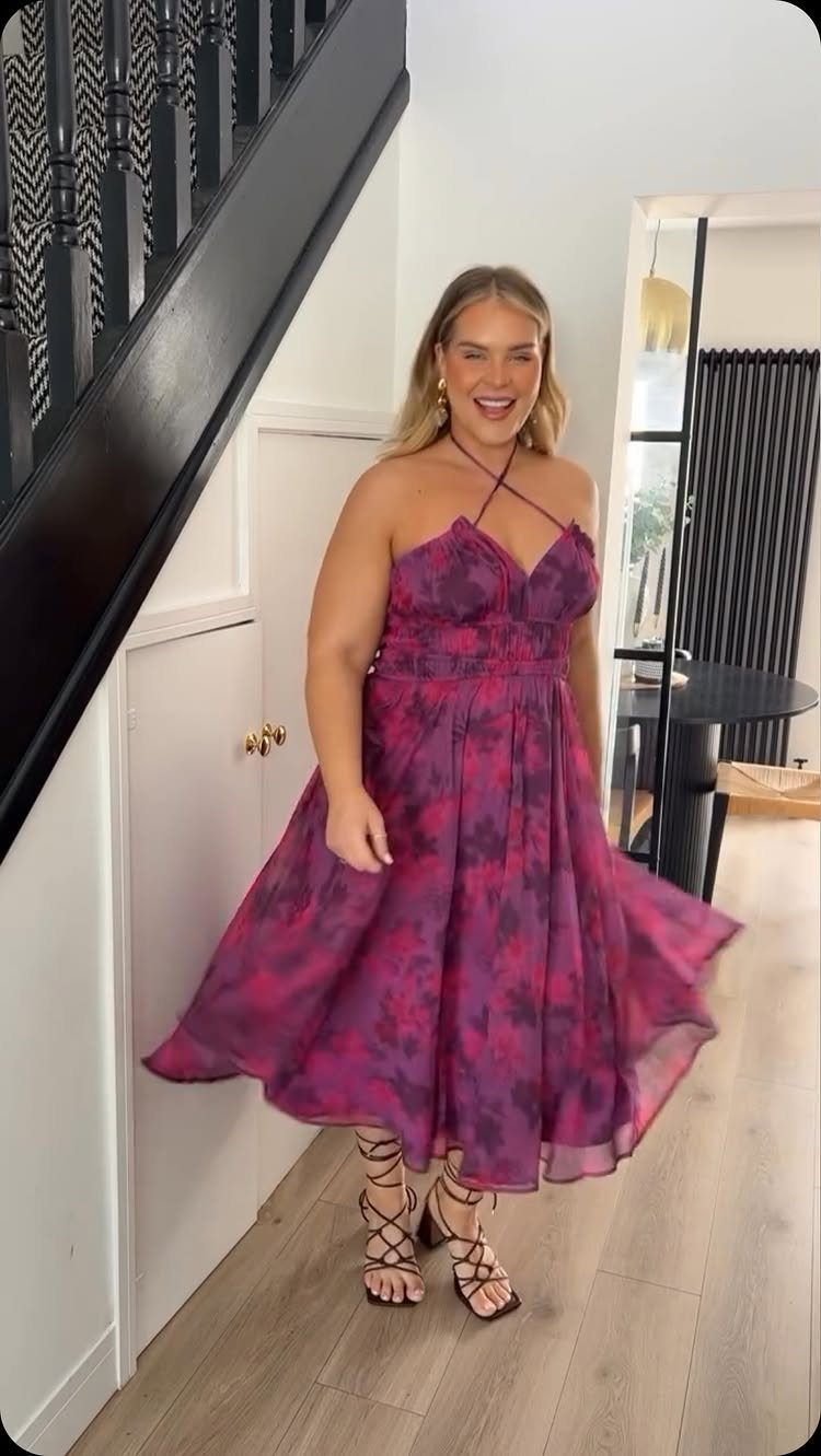 Woman wearing a purple floral print midi dress and lace-up sandals indoors.