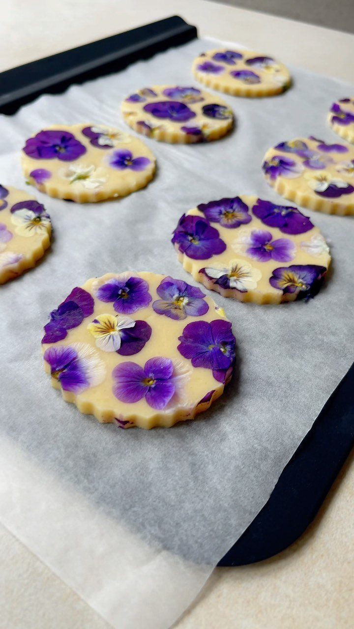 Round yellow cookies topped with purple and white edible pansy flowers on parchment.