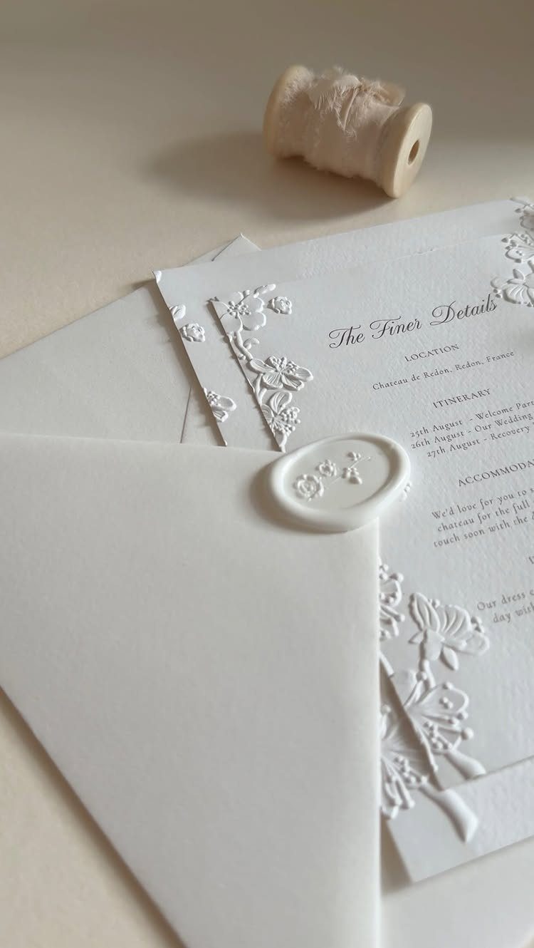 White embossed floral invitations with a wax-sealed envelope and white twine spool.