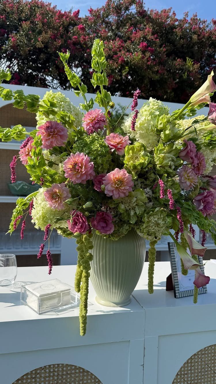 Large floral arrangement with pink and white flowers in a green vase outdoors.