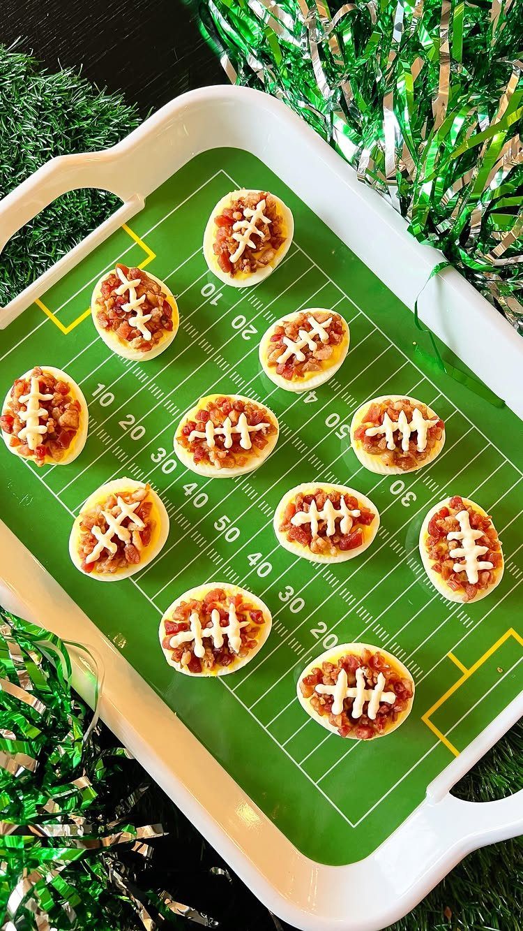 Football-themed deviled eggs on a green football field tray with green tinsel.