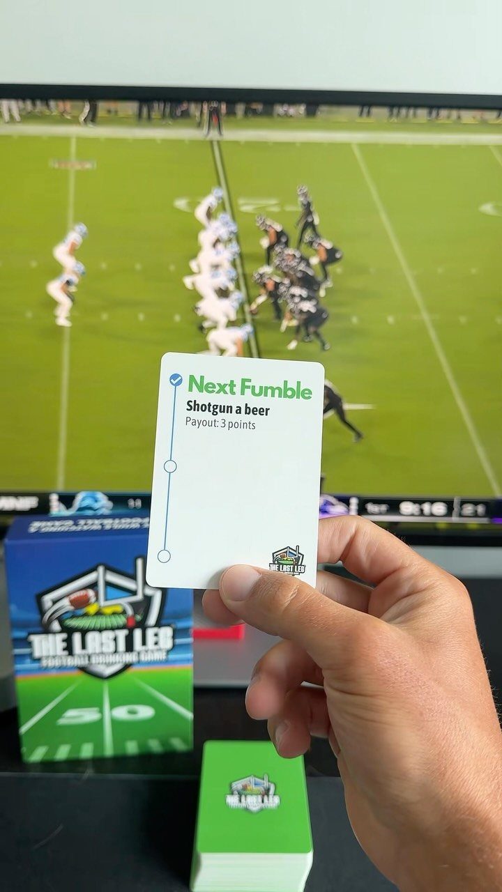 Hand holding a football game card in front of a televised football match.