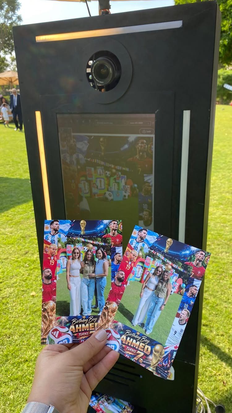 Photo booth kiosk and printed strips with soccer-themed backgrounds on a green lawn