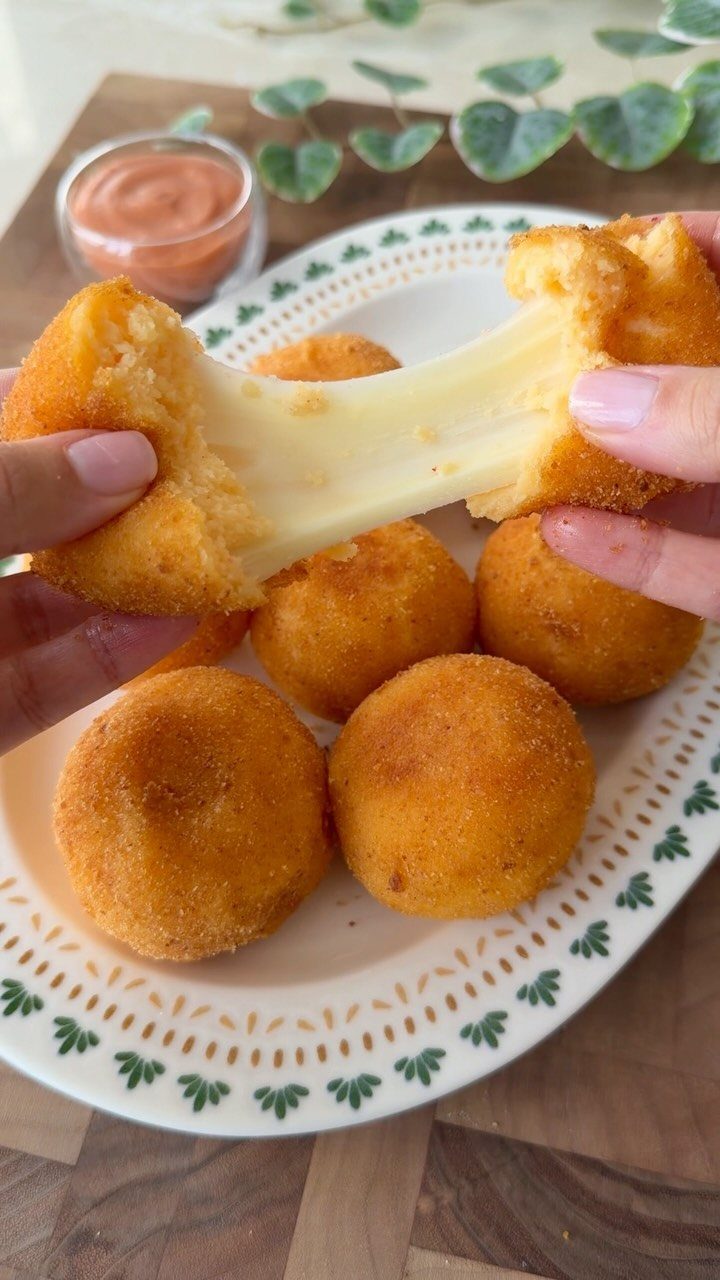 Fried cheese balls on a plate with one being pulled apart showing melted cheese.