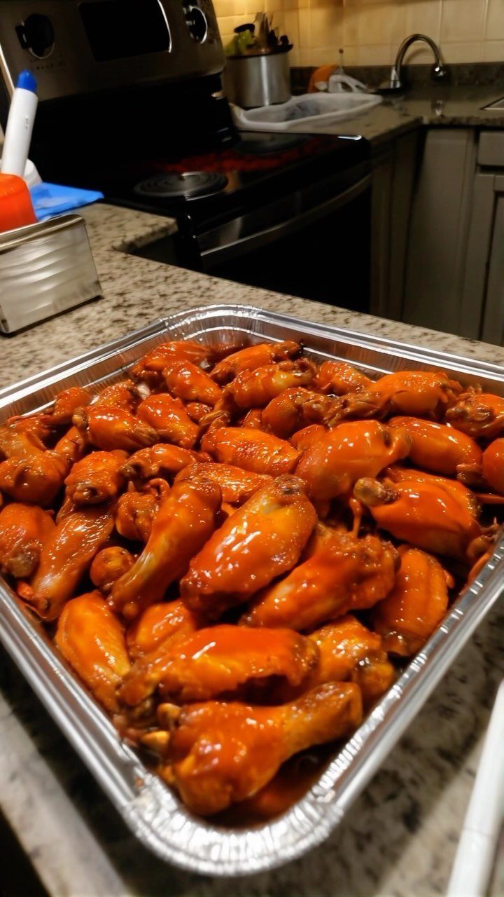 Buffalo chicken wings in a foil tray on a granite kitchen counter.