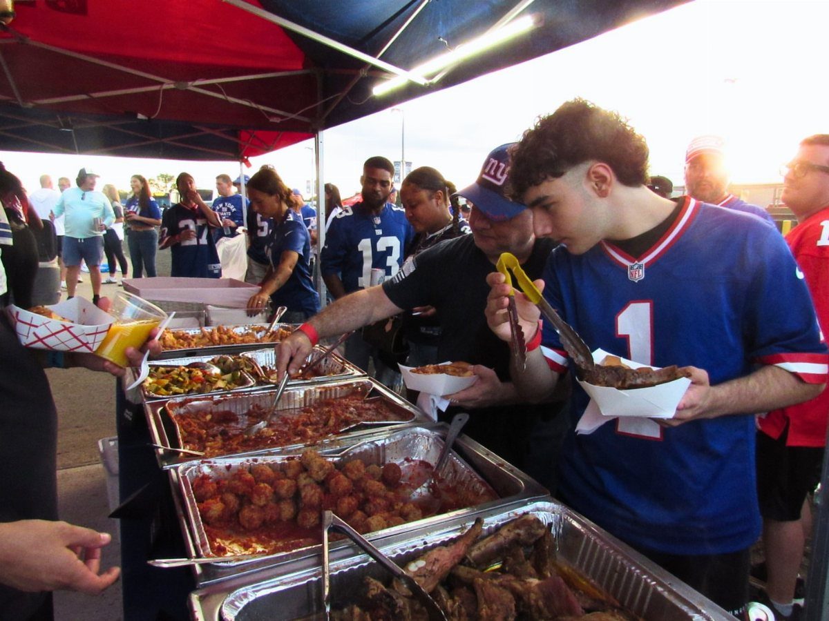 Fans in blue football jerseys eating from food trays at an outdoor tailgate party.