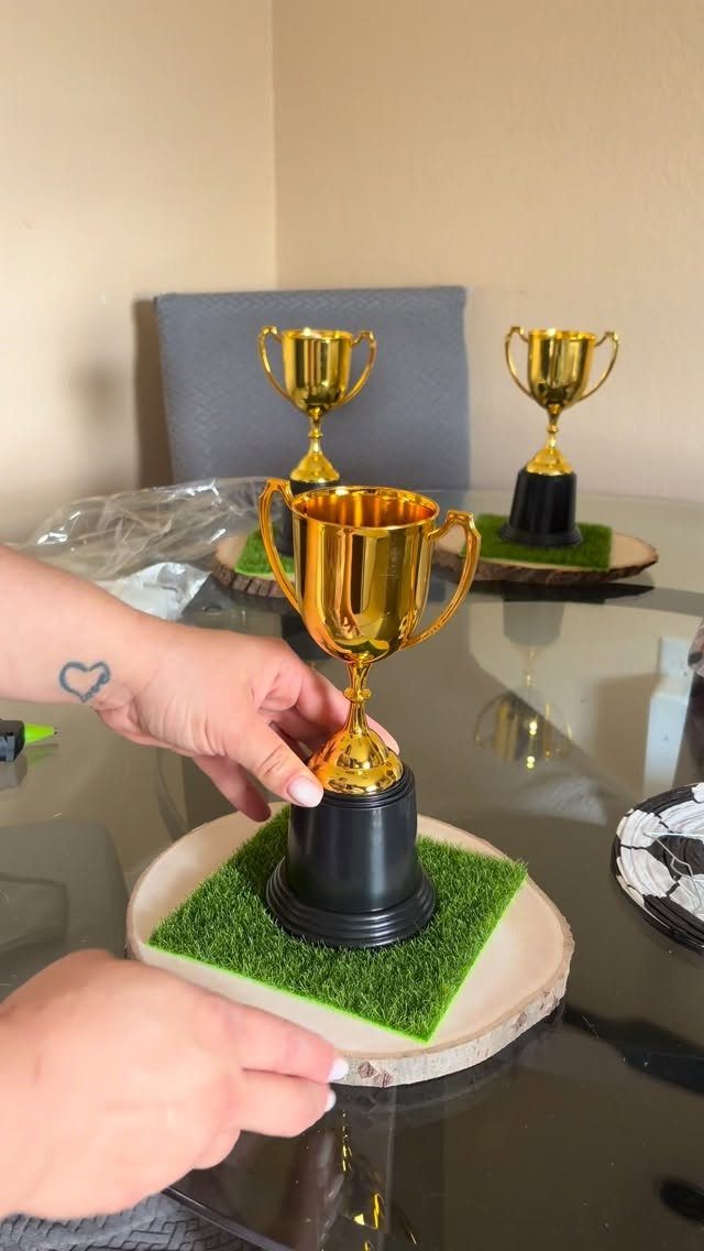 Gold trophies on green turf and wooden slices arranged on a glass table.