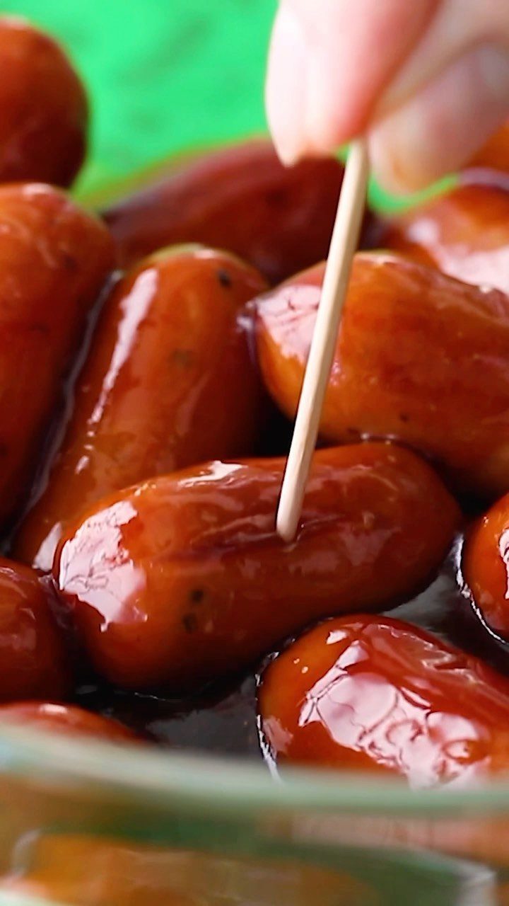 Glazed cocktail sausages being picked up with a wooden toothpick from a dish.