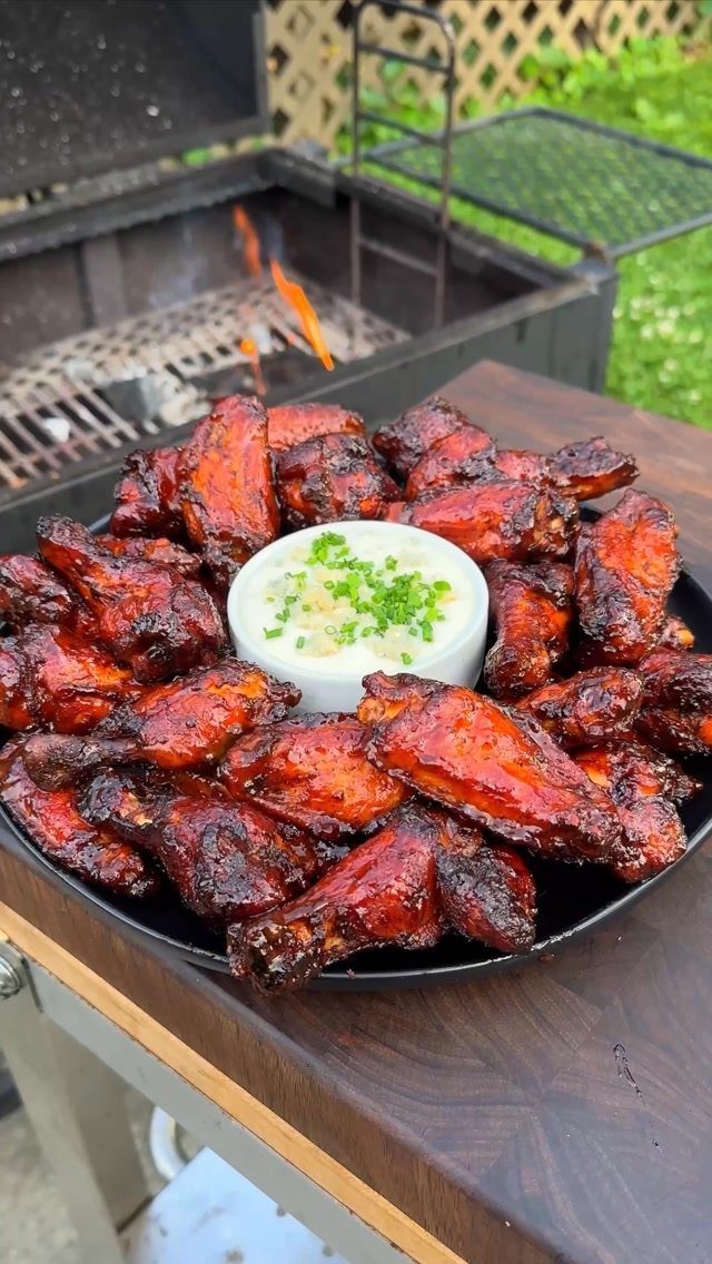 Glazed chicken wings on a black platter with a side of creamy dip.